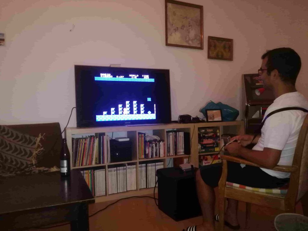 Ein FKR-Mitglied sitzt mit einem Lächeln im Gesicht und dem Controller in der Hand im Wohnzimmer des Vereinsloikals vor dem Bildschirm und steuert Super-Mario.
